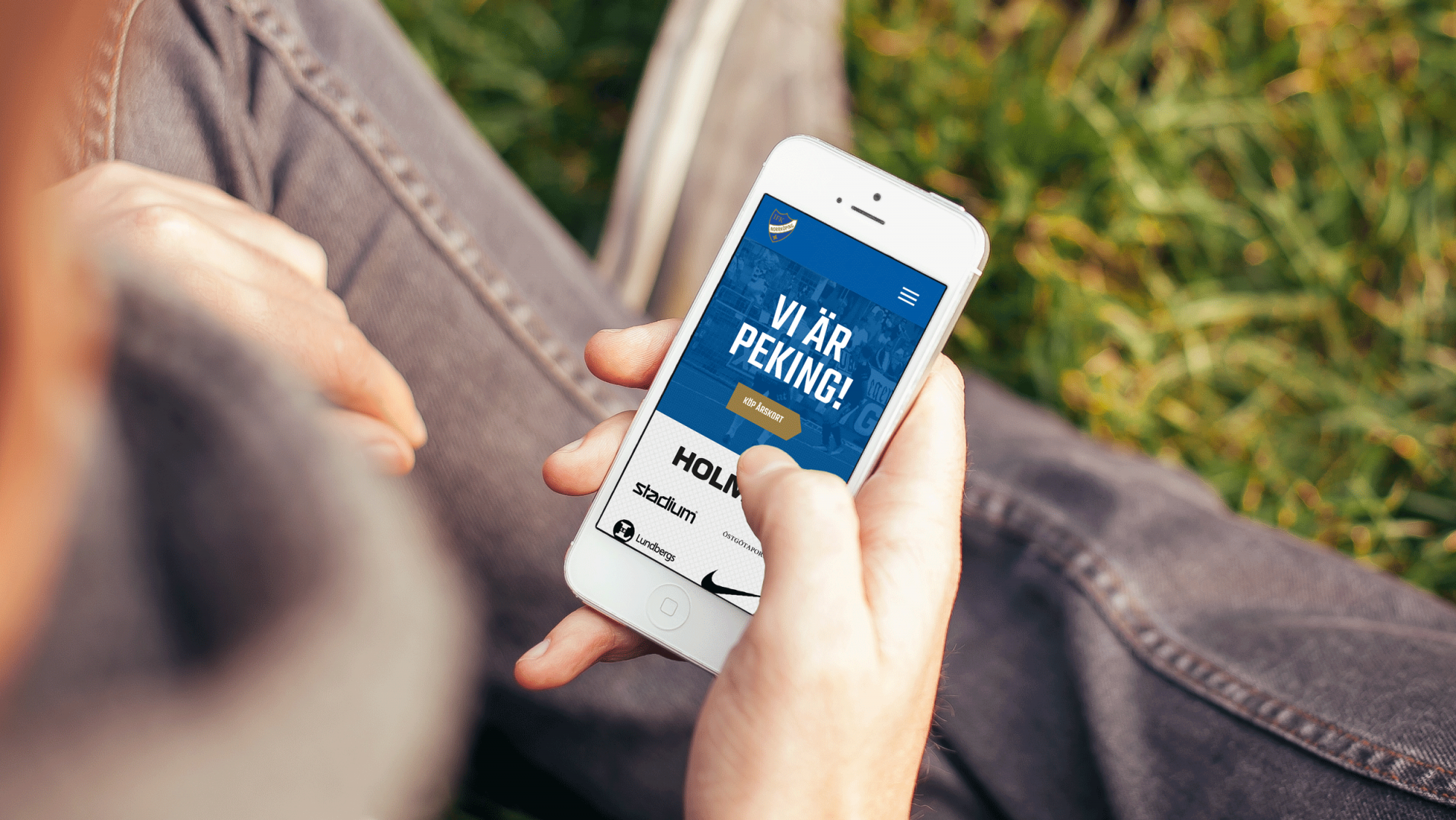 En person håller en smartphone i knät som visar startsidan på IFK Norrköpings nya hemsida